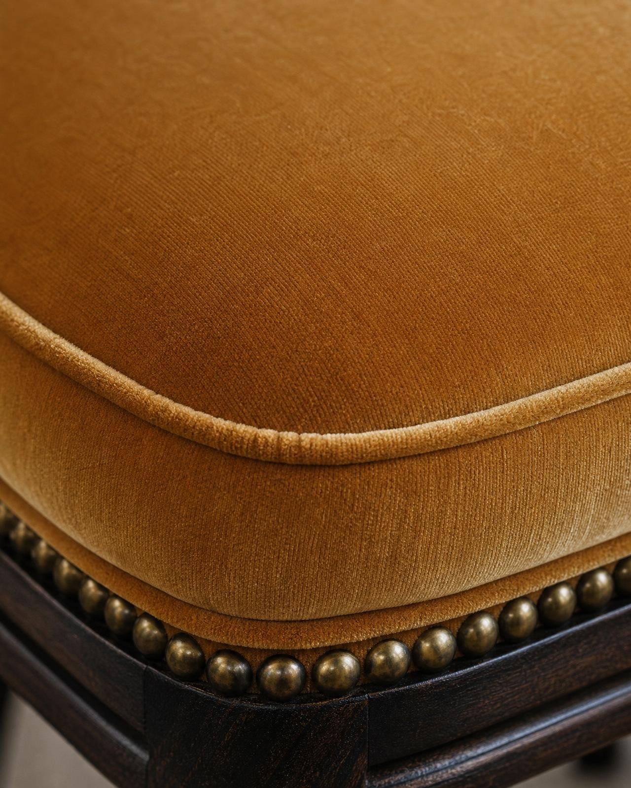 Macro of warm camel velvet dining chair seat with piping and brass nailhead detail