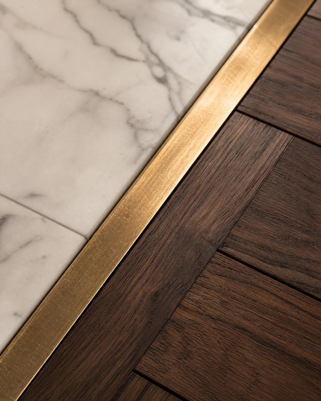Macro of brushed brass inlay strip between marble and walnut parquet flooring