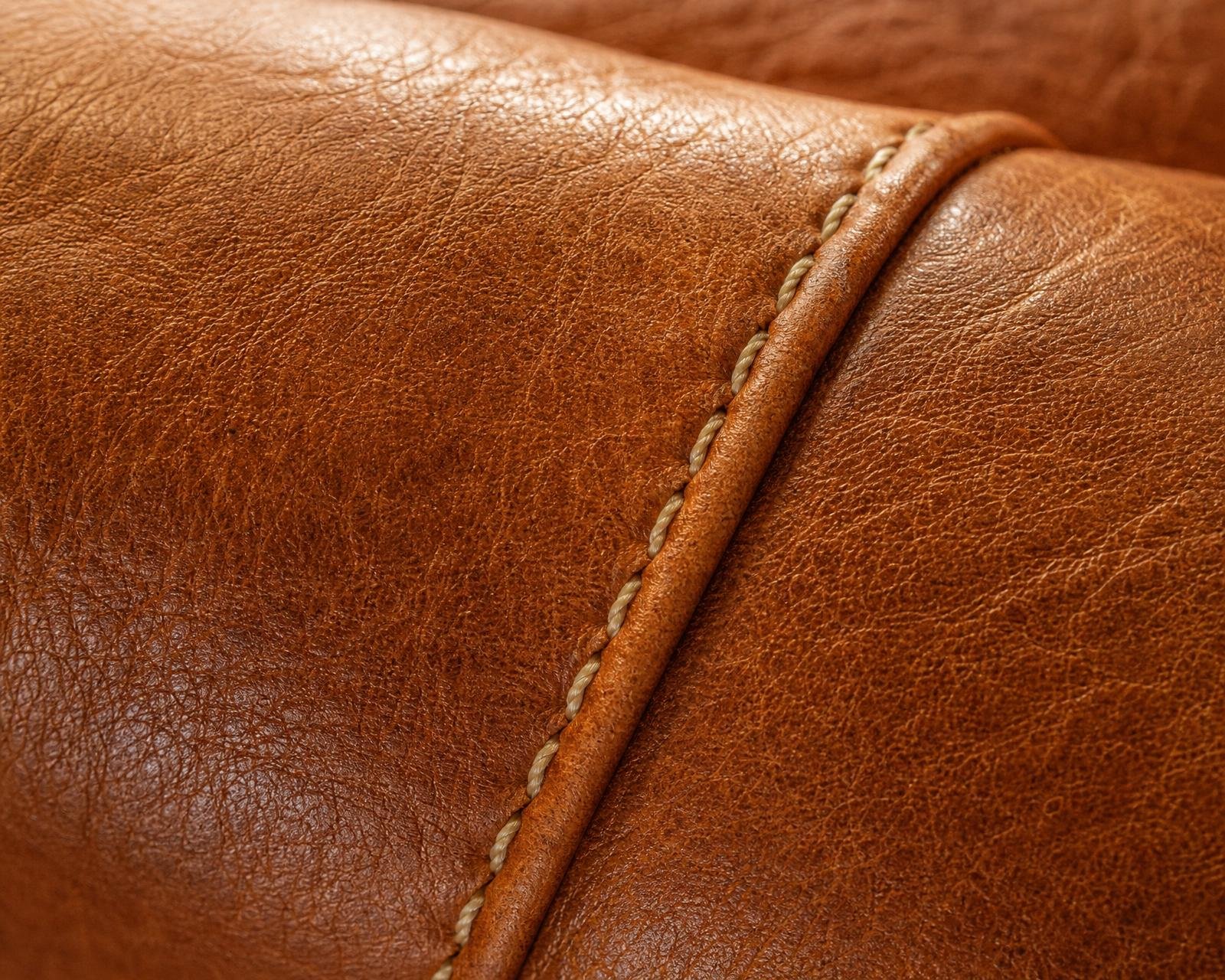 Macro of saddle-tan leather upholstery with natural grain and hand-stitched seam